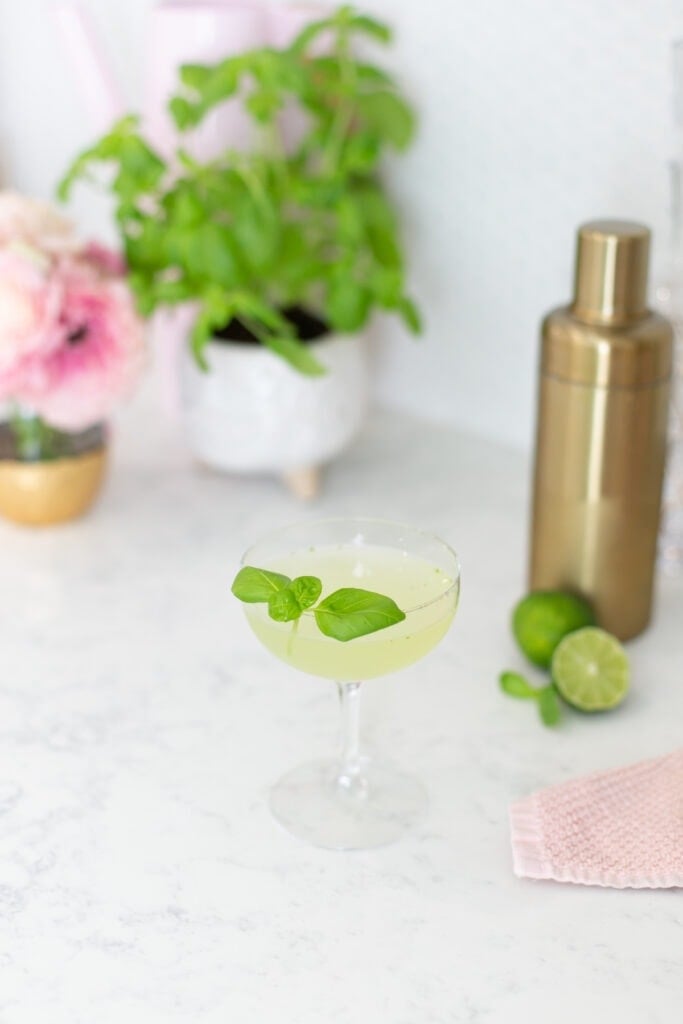 basil gimlet cocktail on a counter with flowers