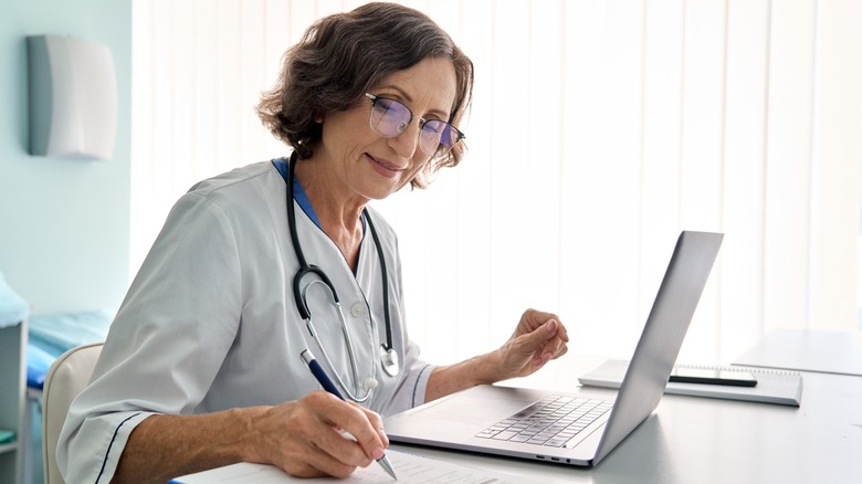 Doctor using laptop and writing